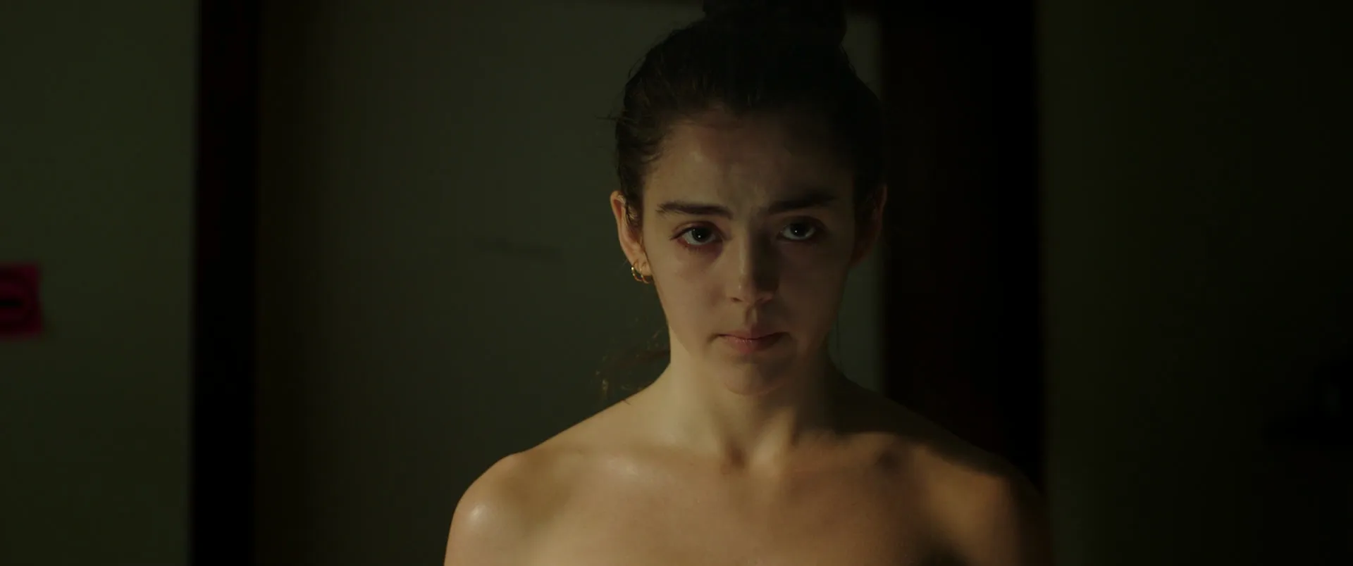 Portrait à mi-corps d'une jeune femme aux épaules nues dans une pénombre verdâtre, une seule lumière rasante sur le visage.