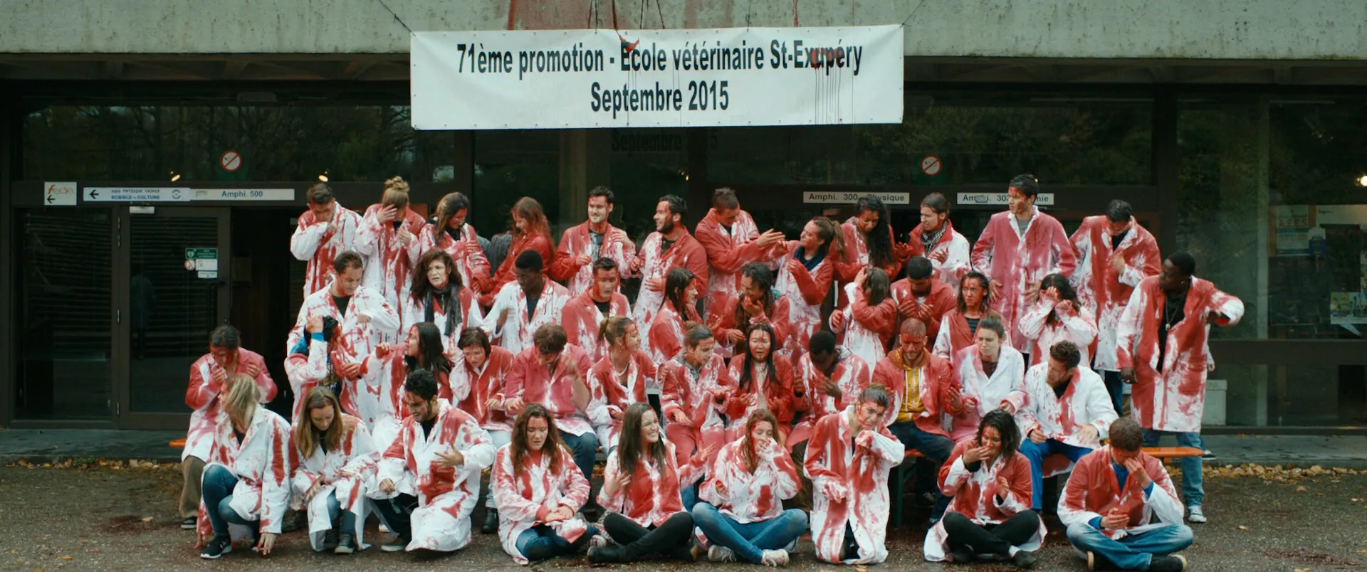 Photo de promotion d'une école vétérinaire : une cinquantaine d'étudiants en blouses maculées de rouge, sous une banderole.