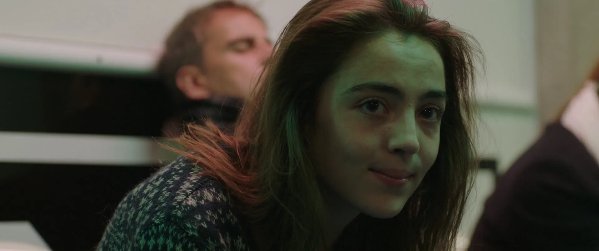 Portrait d'une jeune femme dans un amphithéâtre, la chevelure détourée par une lumière verte de néon.