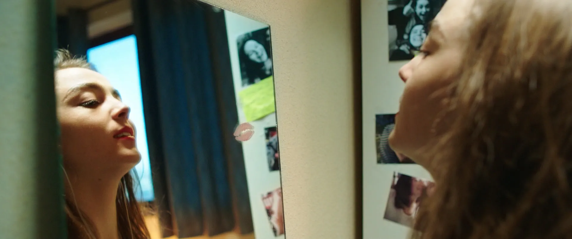Une jeune femme face à un miroir, son profil et son reflet se répondant de part et d'autre du cadre couvert de photos.